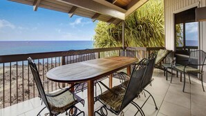 A wooden table and chairs on a balcony with a view of the ocean.