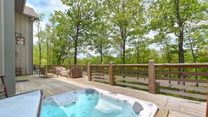 Un jacuzzi en una terraza de madera con un cerco de madera y árboles al fondo.