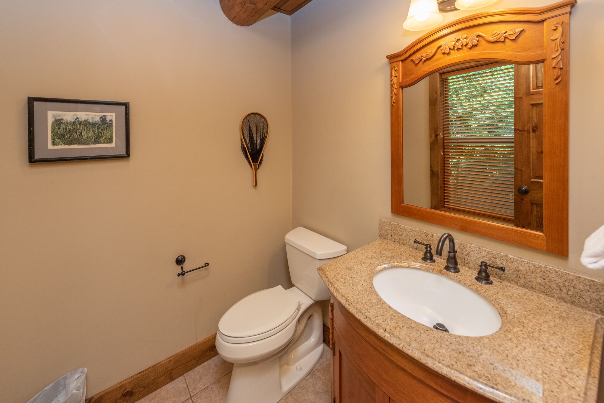 A bathroom with a white toilet, a sink with a wooden vanity, a framed picture on the wall, and a decorative mirror above the sink.