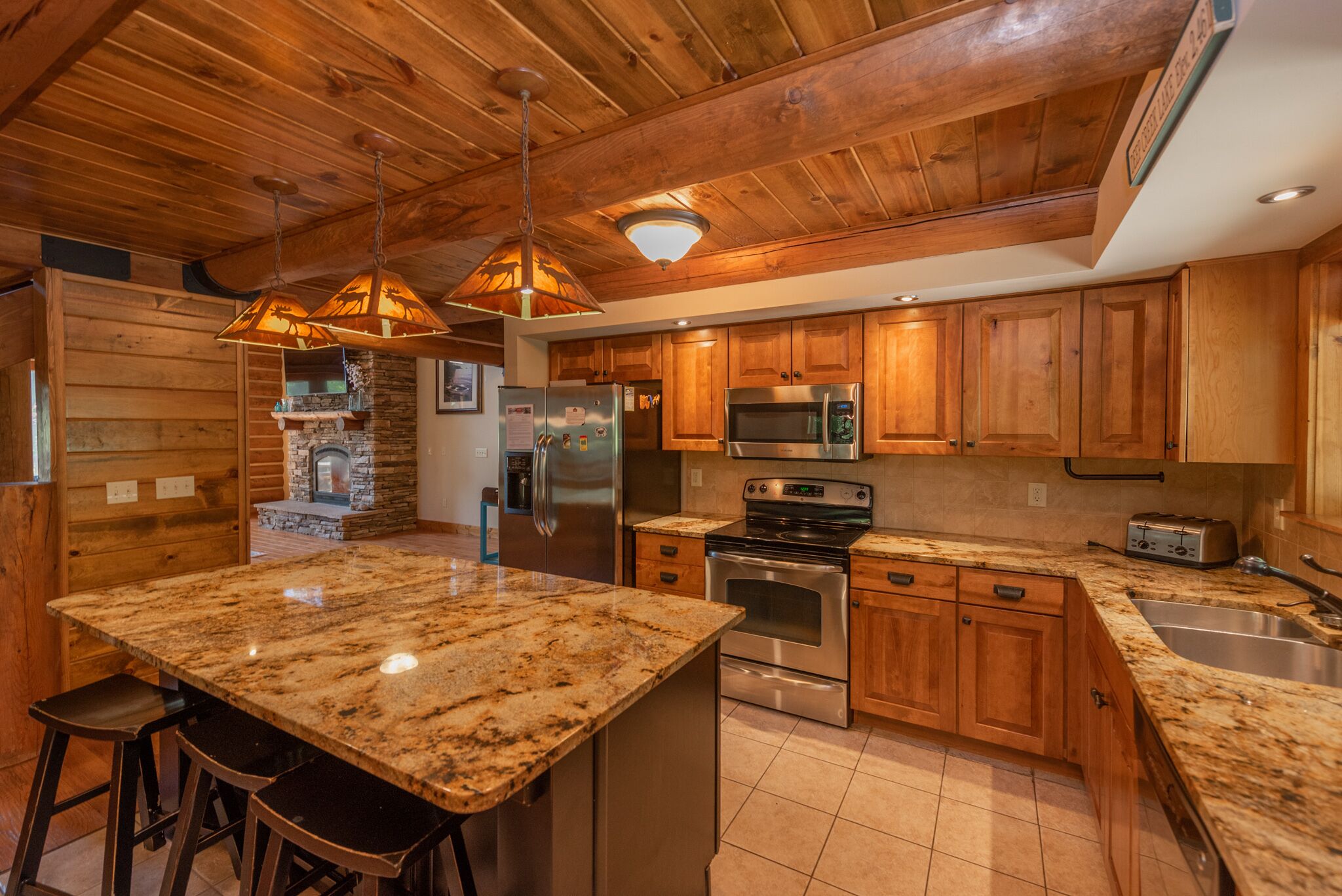A kitchen with wooden cabinets, granite countertops, stainless steel appliances, and a stone fireplace.