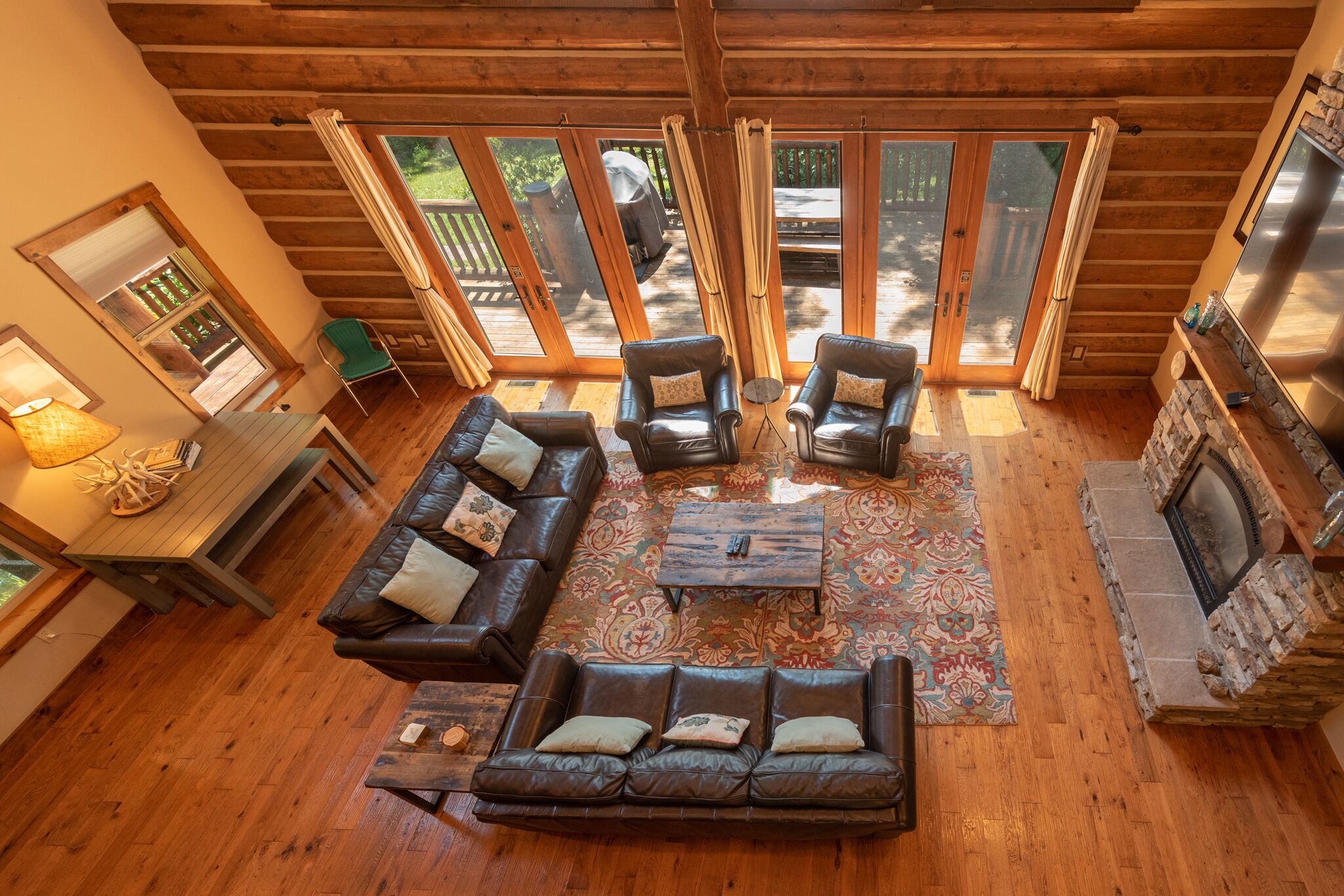 A cozy living room with a fireplace, leather sofas, and a large window overlooking a deck.
