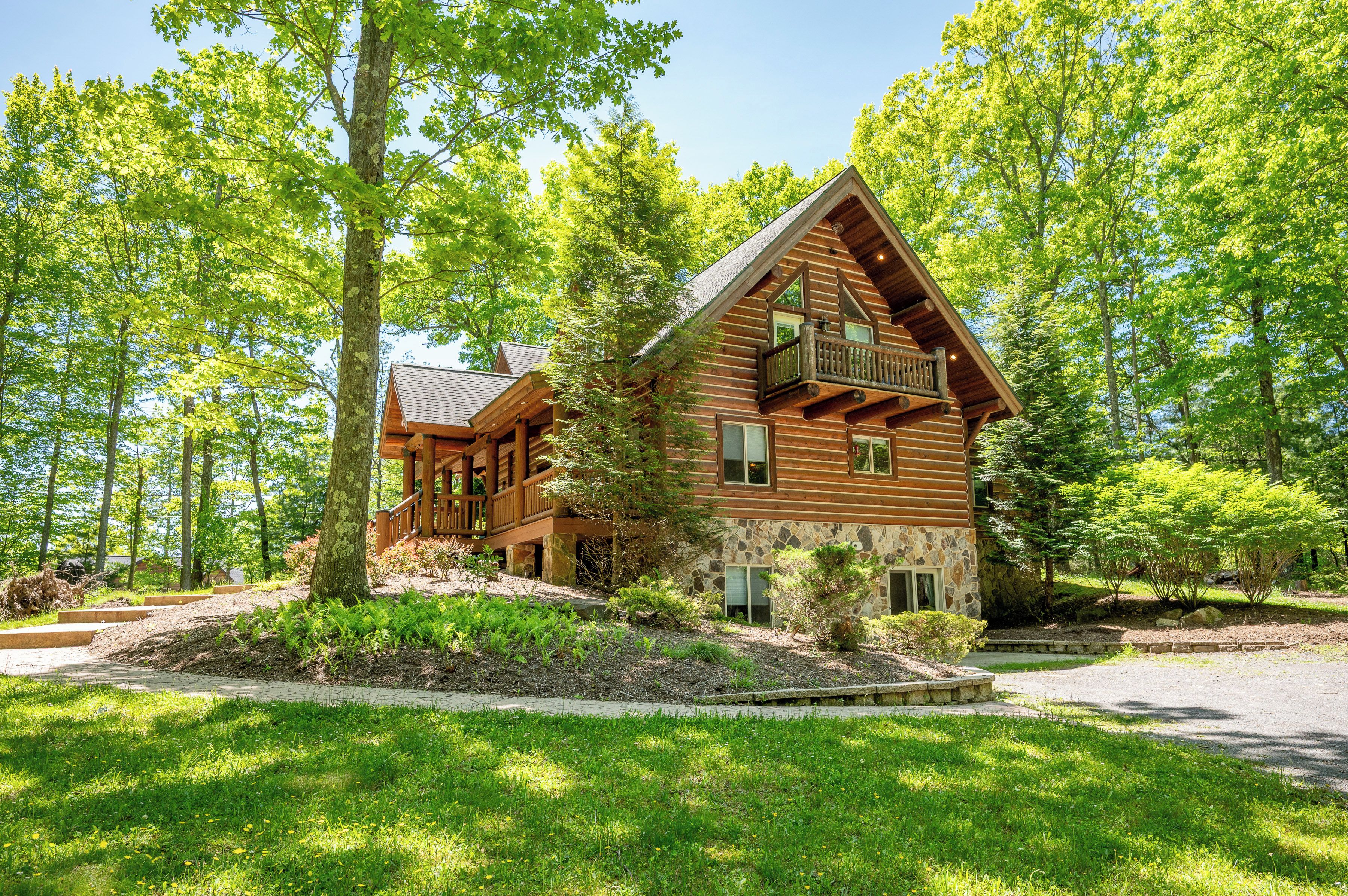 A log cabin with a balcony, surrounded by lush greenery and trees.