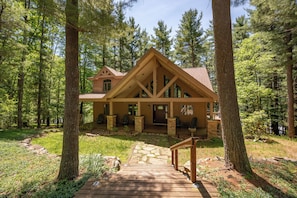 A cabin with a stone foundation, wooden deck, and a staircase leading to the entrance.