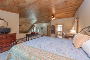 A bedroom with a wooden ceiling, a bed with patterned bedding, a dresser, a television, and a mirror. - Cozy Lakefront Charm w/ Dock & Hot Tub (SWANTON)