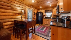 L’intérieur d’une cabane en rondins, avec une table à manger en bois, des chaises, un réfrigérateur, une cuisinière et des armoires en bois.