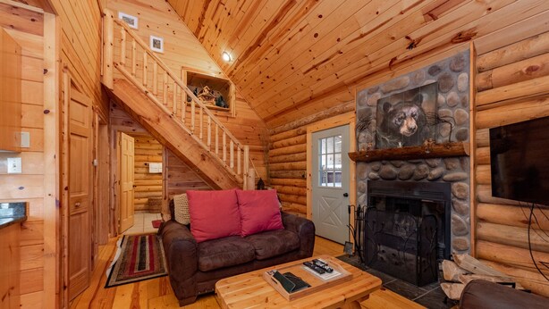 L’intérieur d’une cabane en rondins, avec un escalier en bois, une cheminée, un canapé et une table basse.