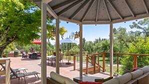 A covered outdoor deck with a seating area, a table, and a staircase leading to a higher level.