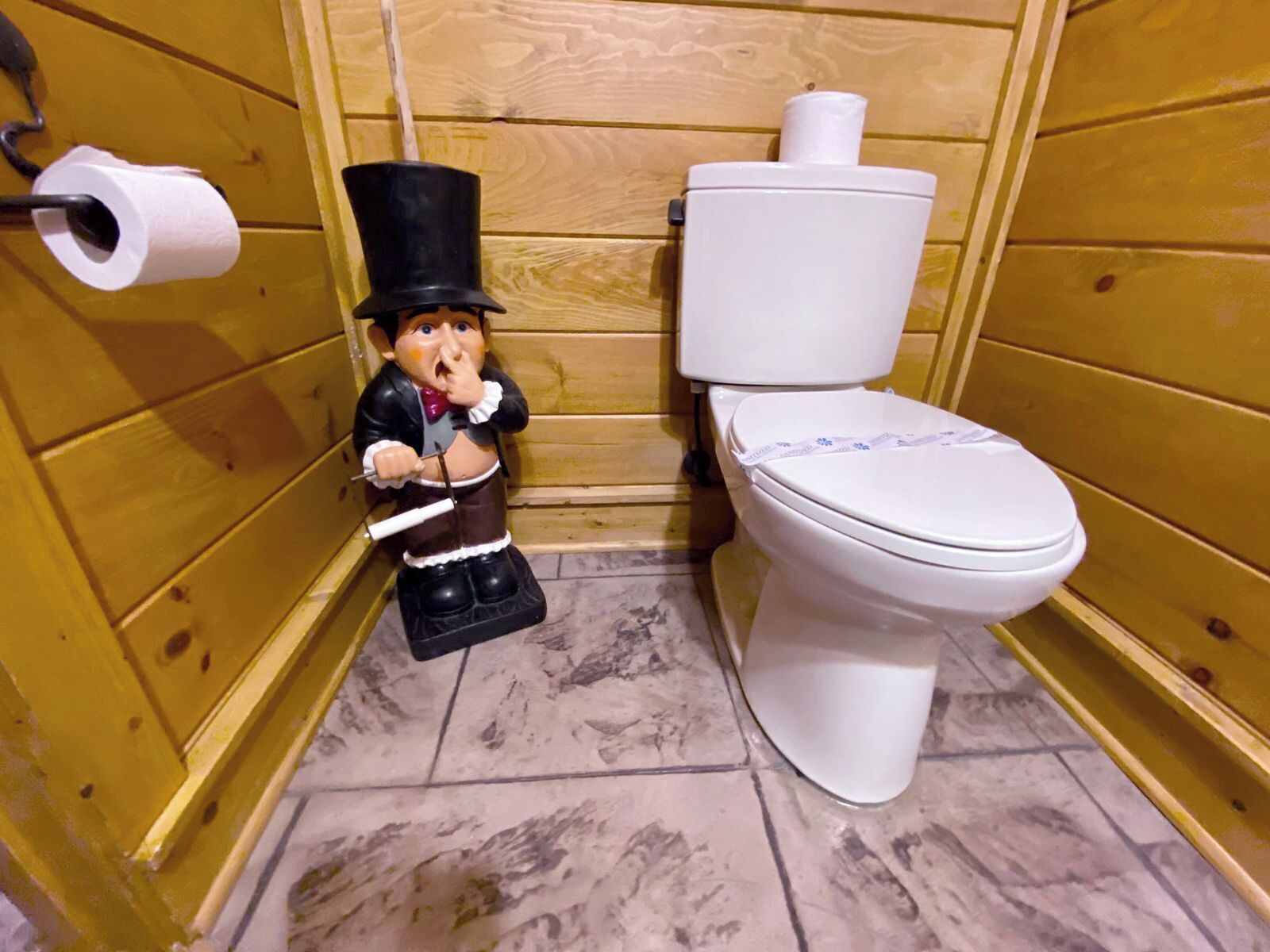A small bathroom with wooden walls, a white toilet, and a toilet paper holder.
