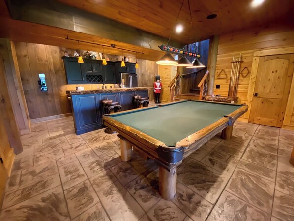 A pool table in a wooden room with a bar area and a figure skater decoration.