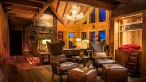 Interior acogedor de una cabaña de madera con muebles de cuero, una araña y una chimenea de piedra.
