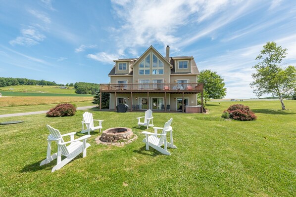 A large house with a balcony, surrounded by a well-maintained lawn and outdoor seating area with Adirondack chairs. - Cozy & Bright Family Fun w/ Pool Table (Swanton)