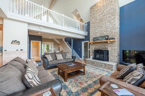 A spacious living room with a high ceiling, a fireplace, a staircase leading to an upper level, and a large window. - Cozy & Bright Family Fun w/ Pool Table (Swanton)