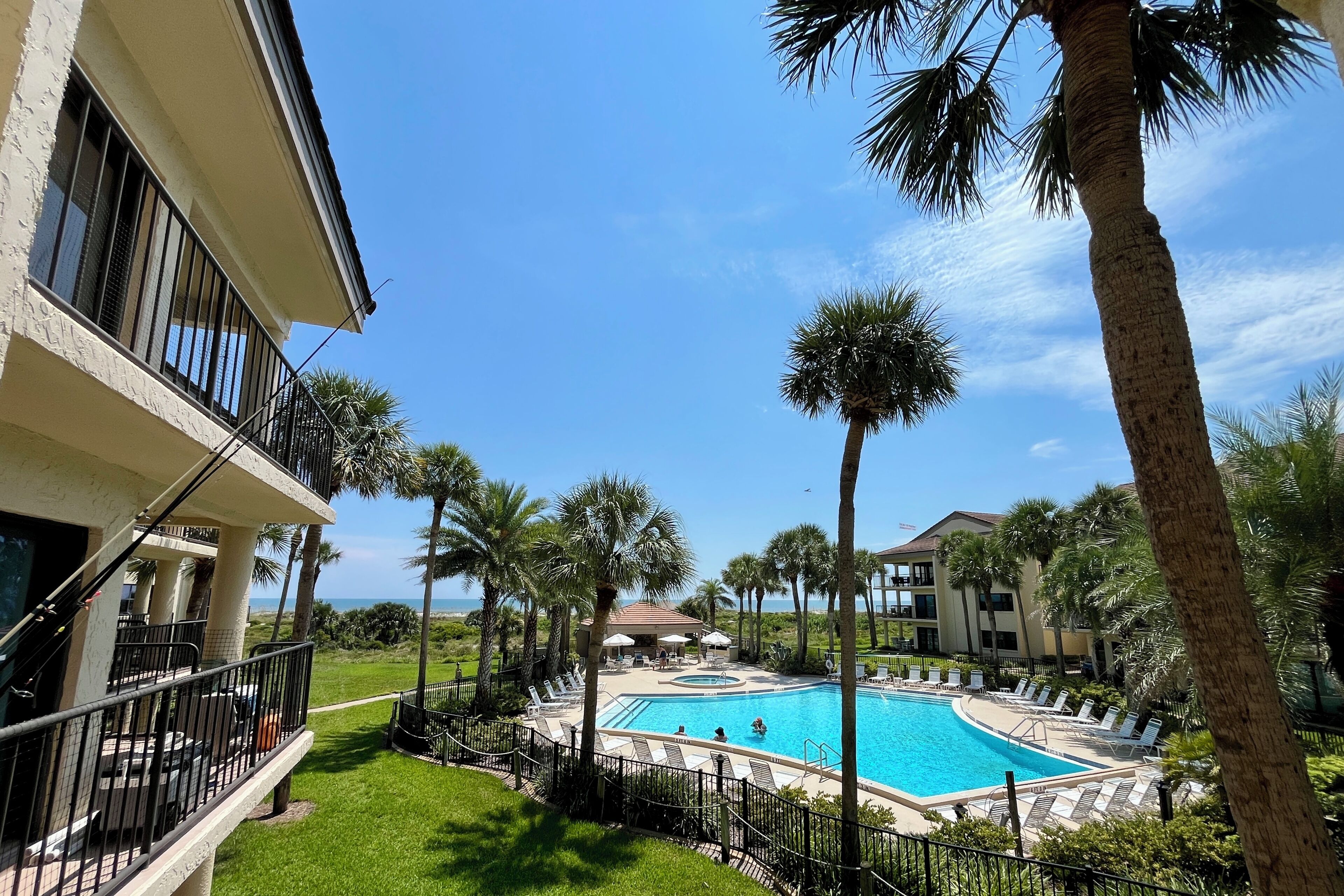 A swimming pool surrounded by palm trees and a building with balconies.