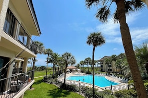 A swimming pool surrounded by palm trees and a building with balconies. - Enjoy a relaxing view of the pool and ocean in the comfort of your private balcony! (Saint Augustine)