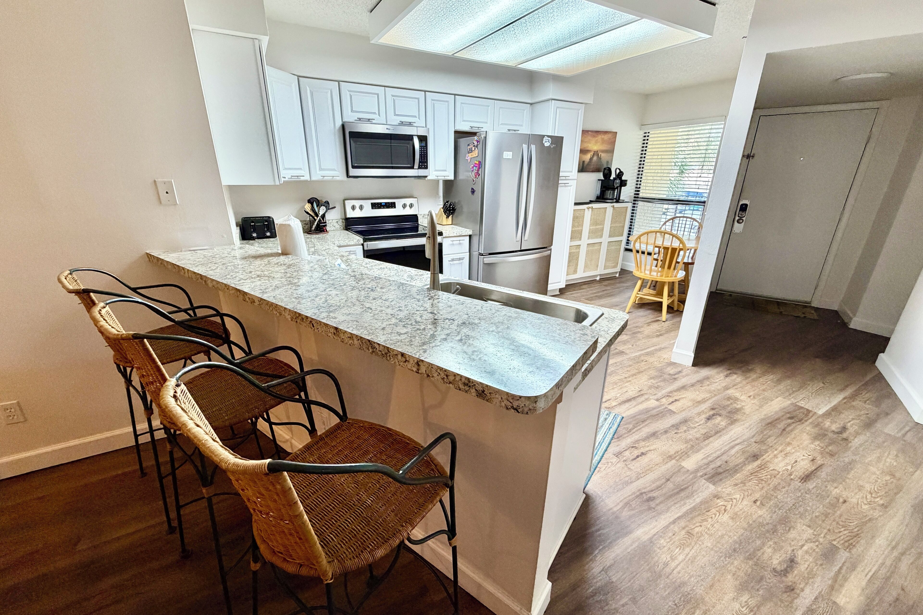 A modern kitchen with a central island, bar stools, and a view of the dining area.