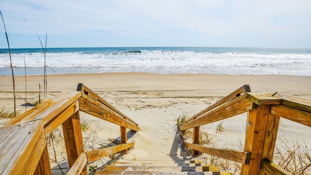 Een houten trap die naar een zandstrand leidt, met de oceaan op de achtergrond.