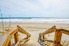 A wooden staircase leading to a sandy beach with the ocean in the background. - Sandstep 616 1 (Carolina Beach)