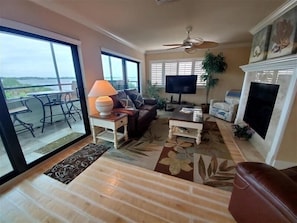 Un salon comprenant un canapé, une table basse, un téléviseur et un balcon aménagé avec du mobilier d’extérieur.