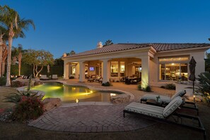 Une maison avec une piscine, un espace extérieur aménagé pour s’asseoir et une terrasse bien éclairée.