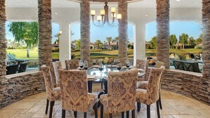 A dining area with a round table, patterned chairs, and a view of a golf course. - FALL FLASH SALE -Luxe Pool, Misters Firepit Lounge & Billiards (La Quinta)