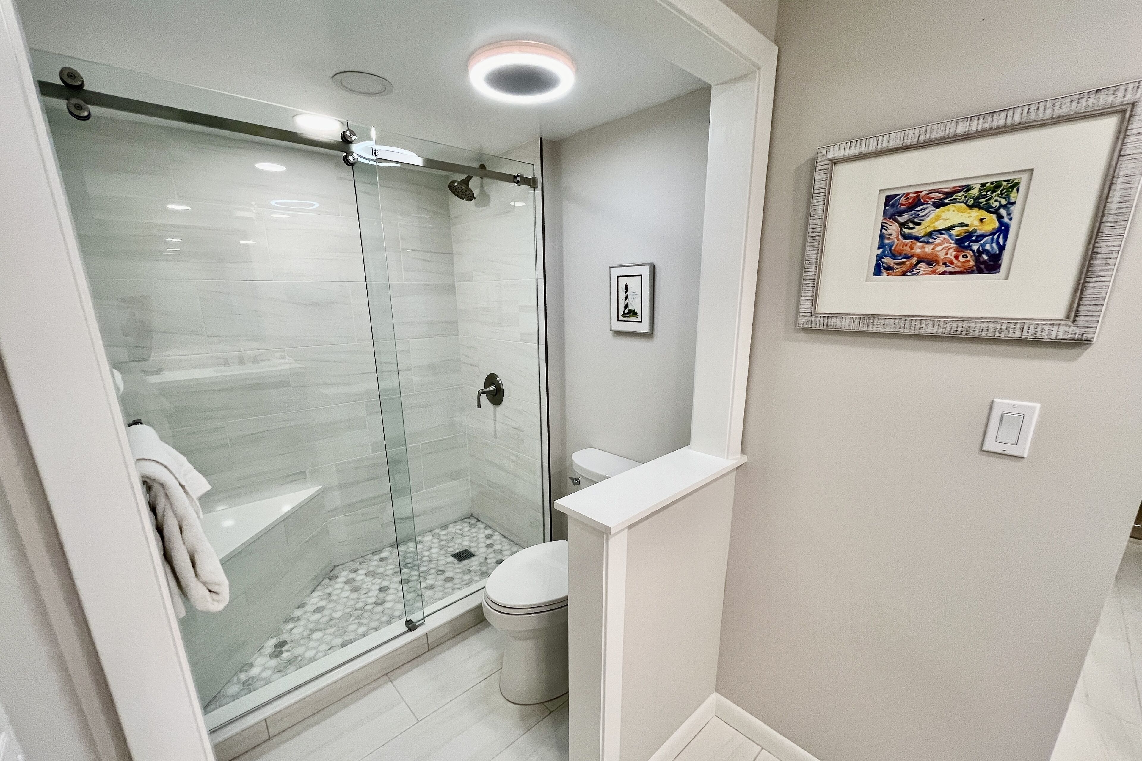 A modern bathroom with a glass-enclosed shower, a toilet, and a framed artwork on the wall.