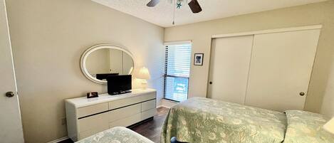 A bedroom with two beds, a ceiling fan, a dresser with a mirror, and a window with blinds.