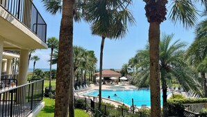 A pool area with palm trees, a building with a balcony, and a view of the ocean. - Soak up the Florida sunshine in this spacious poolside condo with views of the ocean. (Saint Augustine)