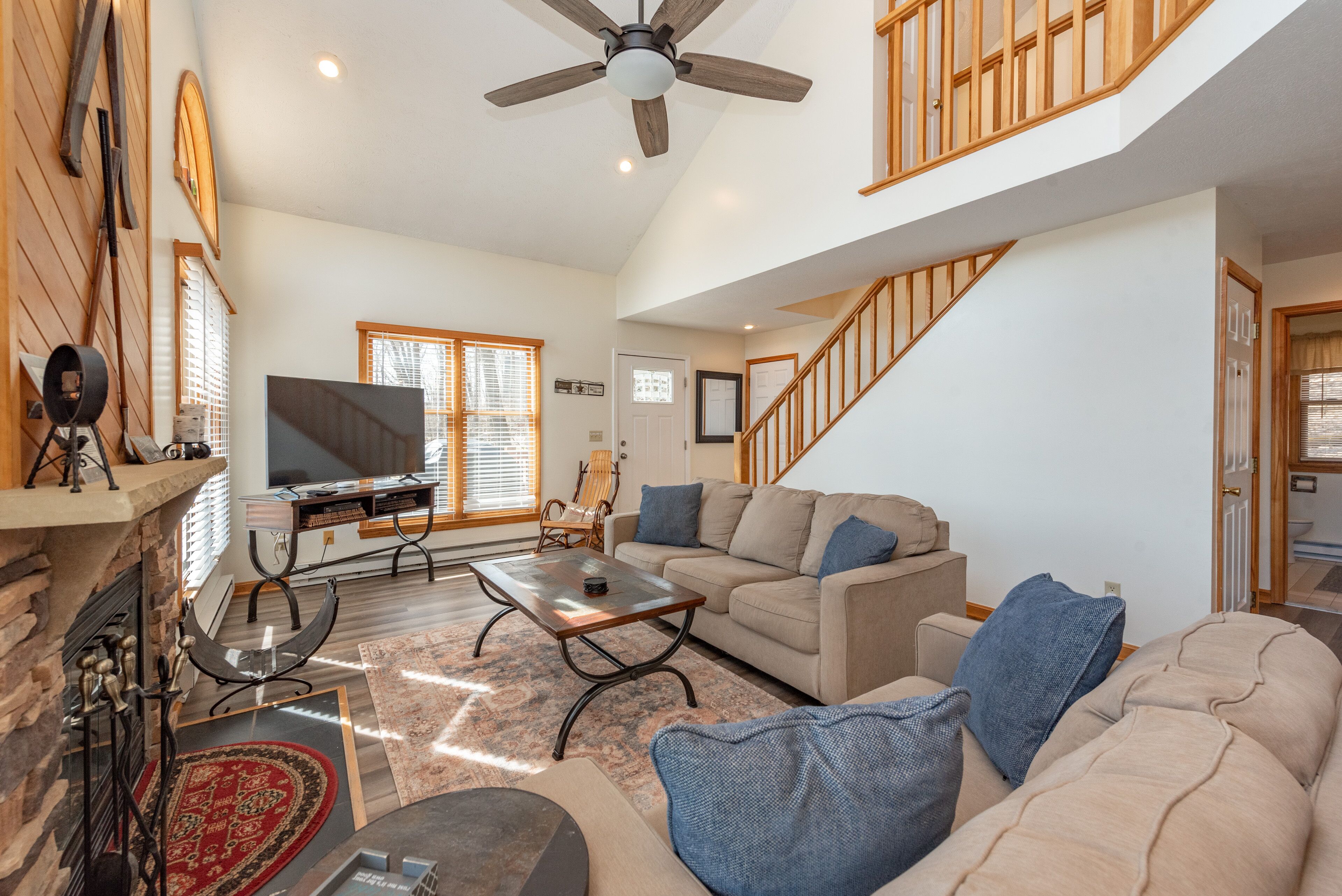 A spacious living room with a fireplace, a large flat-screen TV, a sofa, and a staircase.