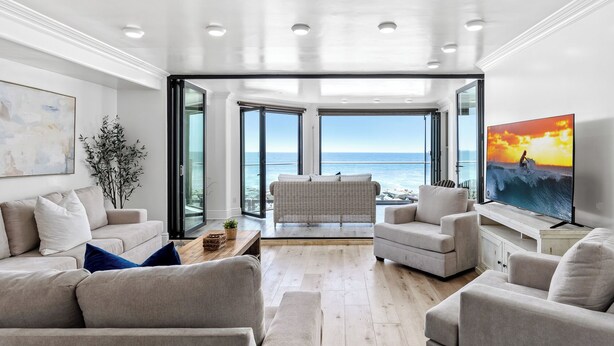 Ett modernt vardagsrum med utsikt över havet, inrett med en soffa, fåtöljer, ett soffbord och en tv.