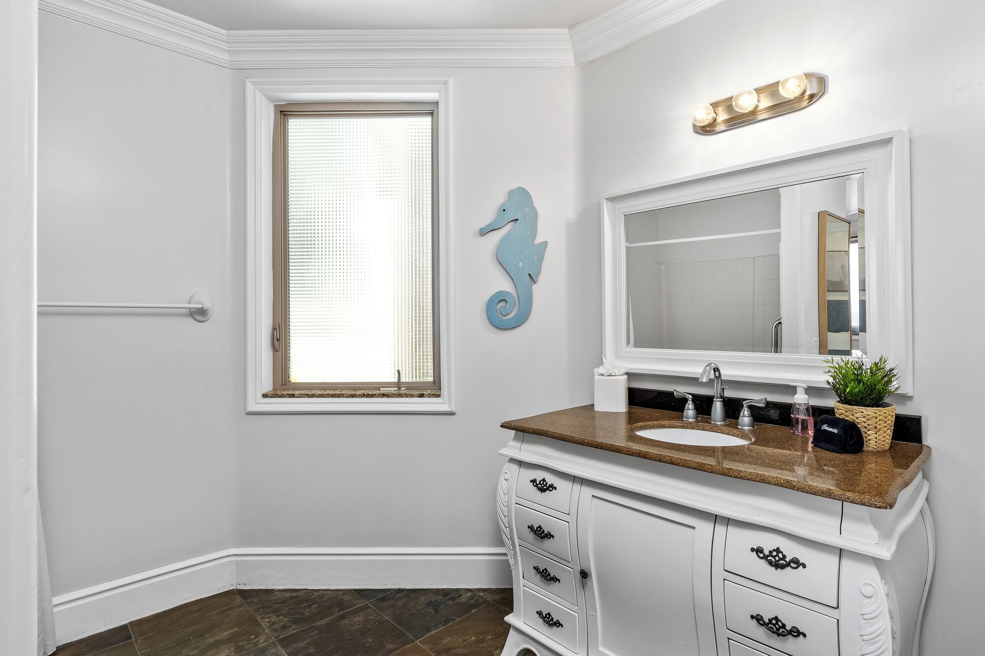 A bathroom with a white vanity, a large mirror, a seahorse decoration, a window with blinds, and a towel rack.