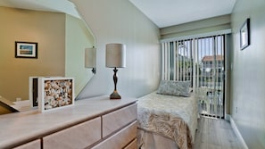 A bedroom with a bed, a nightstand, a lamp, a framed picture, and a window with a view of buildings.