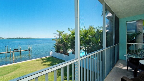 A balcony with a view of a calm lake, a grassy area, and a pool.
