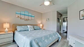 Ein Schlafzimmer mit Bett, Nachttischen, Deckenventilator und Kunstwerken an der Wand.