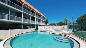 A swimming pool with lounge chairs and a building with balconies. - Pelican Cove 12 -  Anna Maria Island - Across the street from the beach- Condo  2 Bedroom /2 Bath bay view with a community pool,  maximum occupancy of 6 people. (Bradenton Beach)