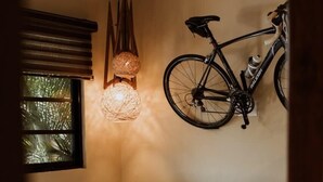 Une pièce comprenant un canapé, une table ronde, un vélo suspendu au plafond, une lampe fixée au mur et une fenêtre avec des stores.