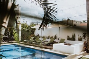 Área de piscina com espreguiçadeiras e uma palmeira.