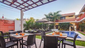 Une terrasse extérieure avec des tables et des chaises, une piscine et un espace salon abrité.
