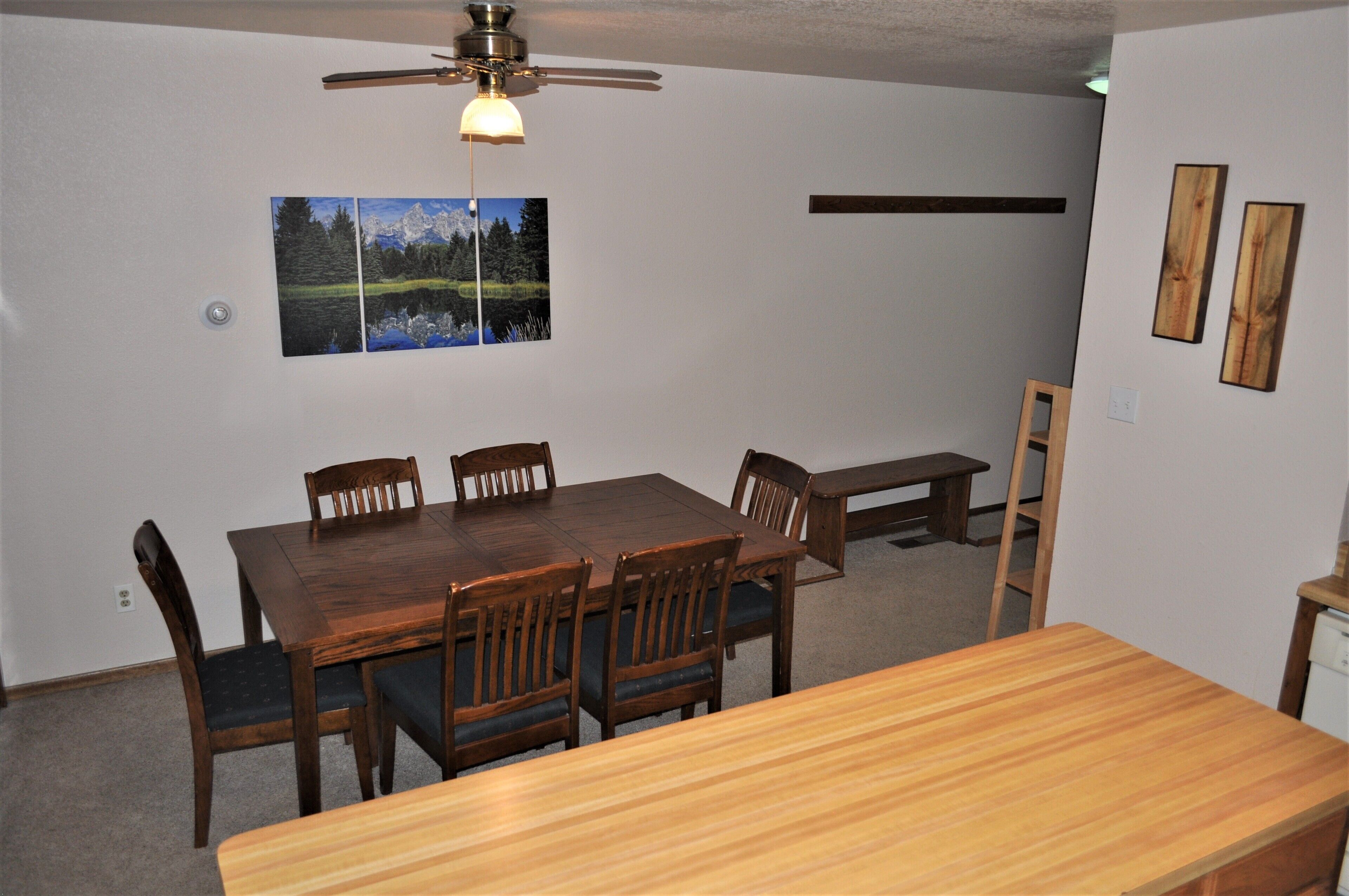 A dining area with a wooden table and chairs, a ceiling fan, and a wall-mounted picture.