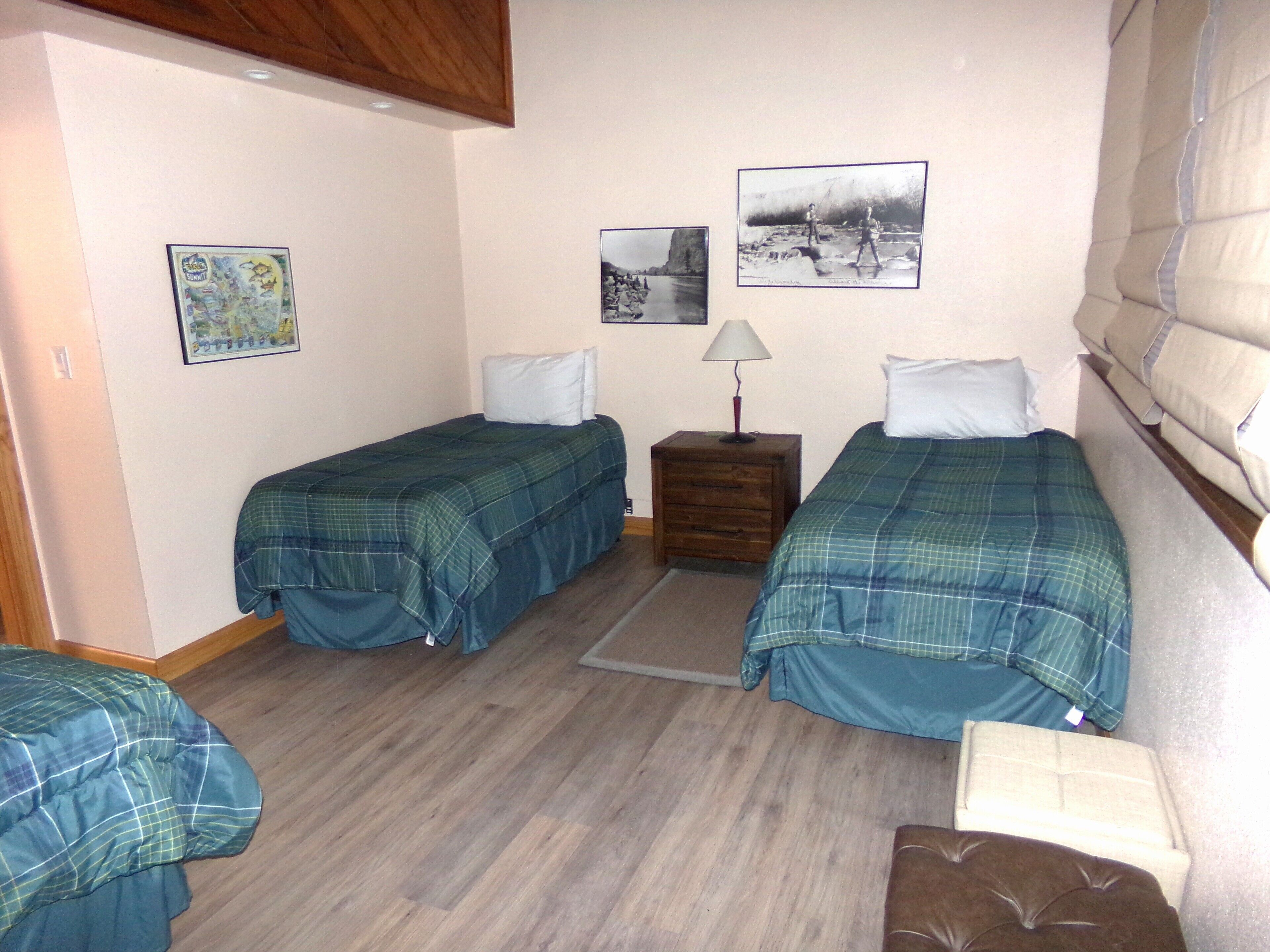 A room with two beds, a nightstand, a lamp, and two framed pictures on the wall.