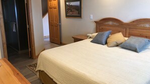 Un dormitorio con una cama de madera, una mesita de noche, un cuadro enmarcado en la pared y una puerta que da a otra habitación.