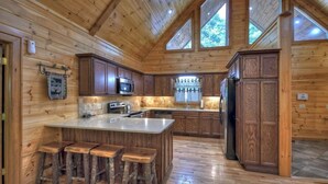 Une cuisine rustique aménagée dans une cabane en bois, avec un îlot central, des tabourets de bar et des appareils électroménagers intégrés.