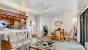 A living room with a sofa, coffee table, dining table with chairs, a ceiling fan, and a kitchen area with cabinets and a refrigerator. - Watch Waves from Lanai w/Wet Bar! Full Kitchen, WiFi, TV, Washer/Dryer Kanaloa 2902 (KAILUA-KONA)