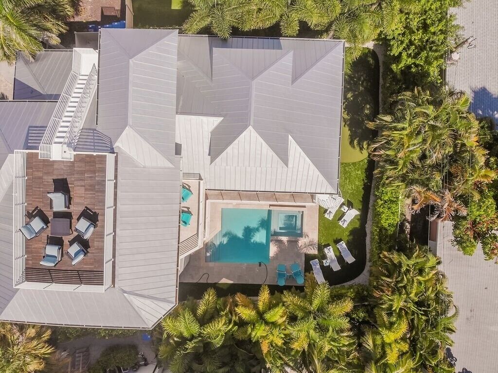 Vista aérea de un hotel moderno con piscina en la azotea, zona de estar cubierta al aire libre y exuberante vegetación circundante.
