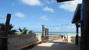 Un camino de hormigón que lleva a una playa con palmeras y un banco de madera.