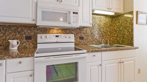 Una cocina con armarios blancos, un microondas, un horno, una encimera de granito y un lavabo de acero inoxidable.