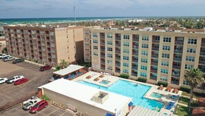 Un hotel con piscina en la azotea, varios balcones y vistas a la playa.