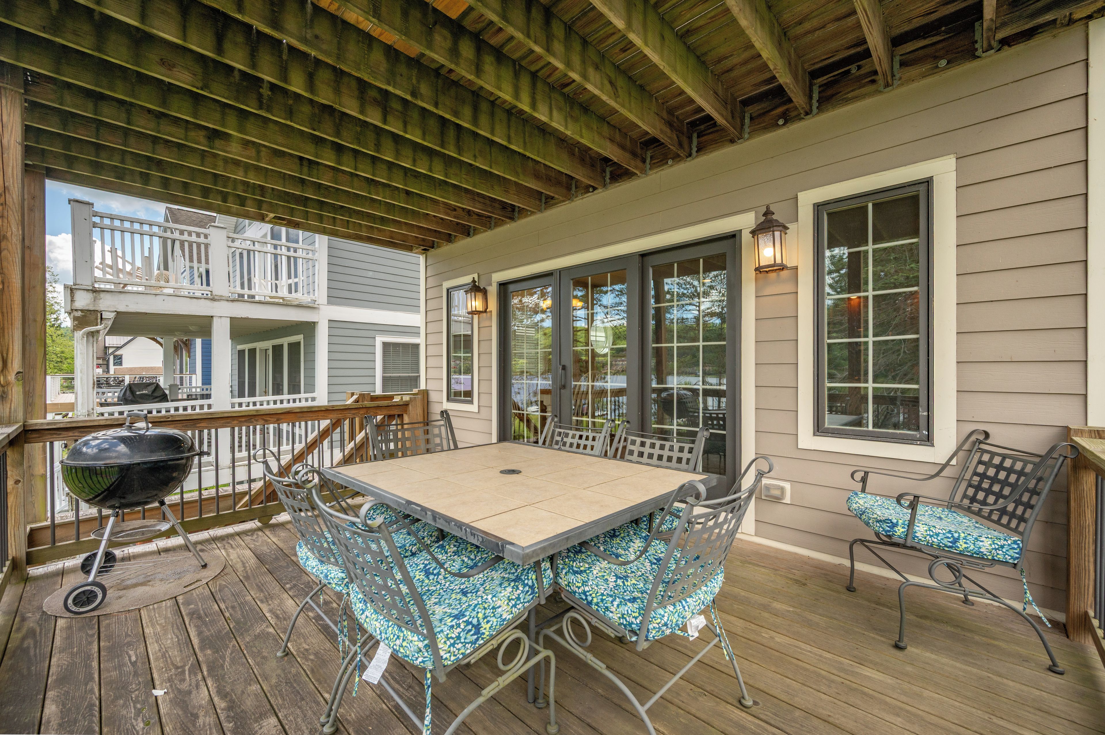 A covered outdoor patio with a table and chairs, a grill, and a view of the house.