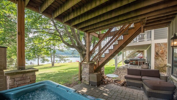 A covered outdoor area with a hot tub, stone pillars, and a staircase leading to a deck with outdoor furniture. - Swim, Ski & Scenic Lake Views by Deep Creek Lake (MCHENRY)
