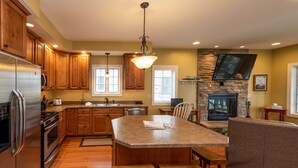 A kitchen with wooden cabinets, a granite island, and a stone fireplace. - Swim, Ski & Scenic Lake Views by Deep Creek Lake (MCHENRY)
