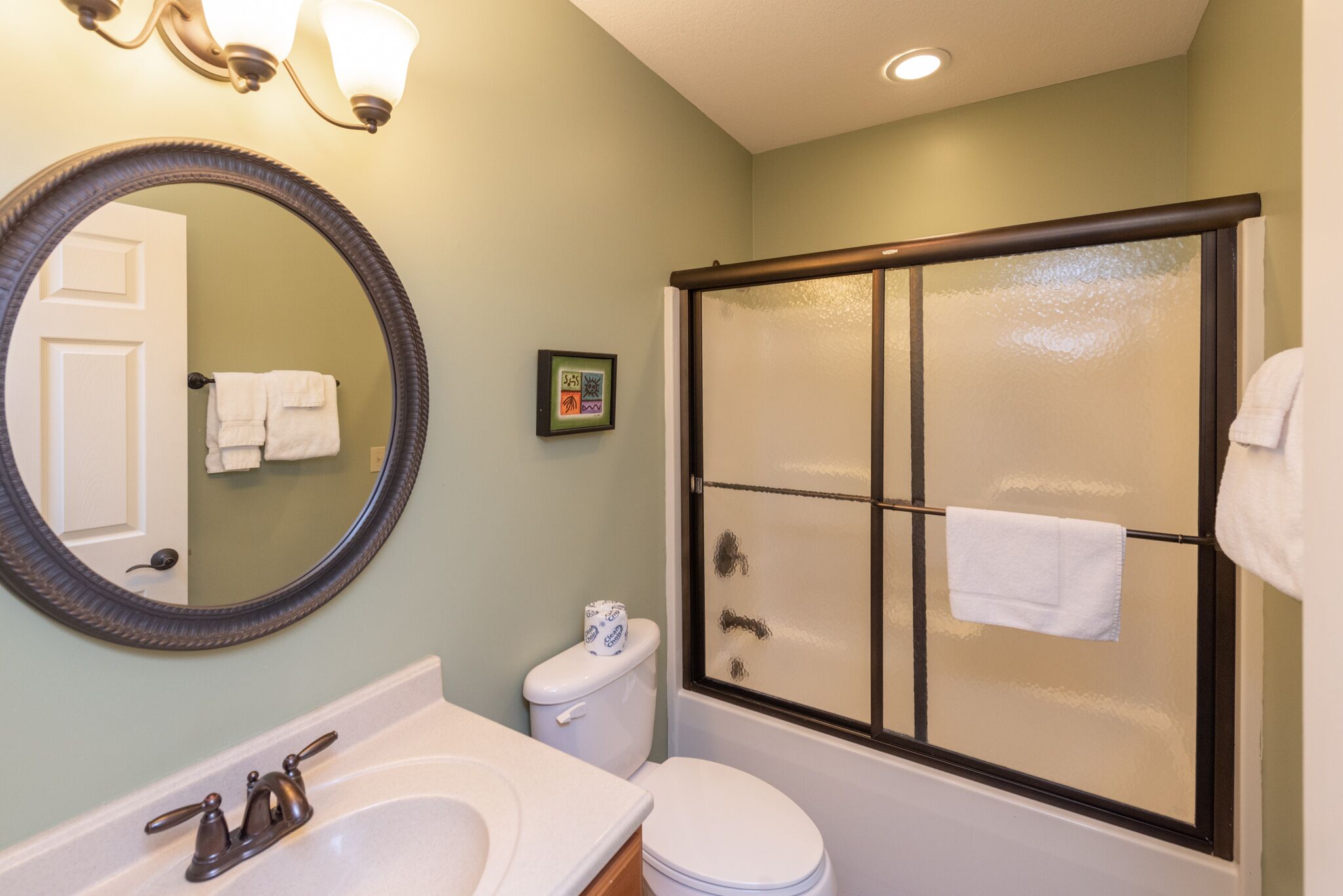 A bathroom with a sink, mirror, toilet, and glass-enclosed shower.